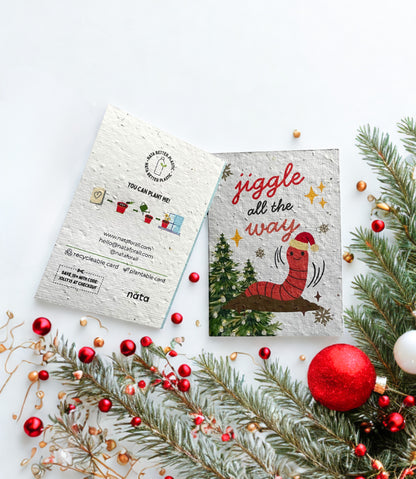 Christmas-themed seed paper card with a worm illustration and festive decorations on a white background.